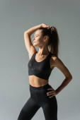 Side view of fit sportswoman in leggings and sports bra looking away and while standing on grey  Poster #664862474