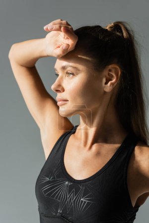 Portrait of sportswoman in modern sports bra looking away isolated on grey, active lifestyle