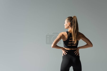 Téléchargez les photos : Sportive tenant la main sur les hanches et se tenant isolée sur le gris, concept de mode de vie actif, athlétique - en image libre de droit