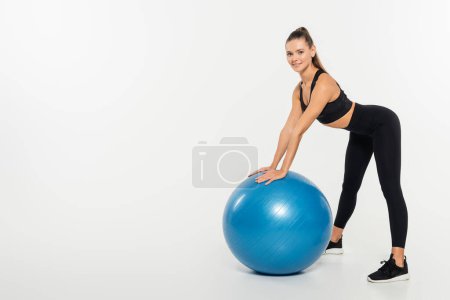 brunette sportswoman looking at camera while standing near fitness ball on white background 