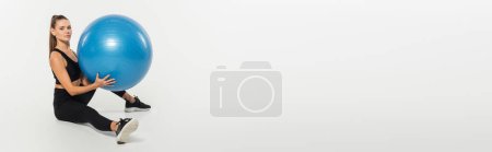 Téléchargez les photos : Femme en soutien-gorge de sport noir tenant balle de fitness et regardant la caméra sur fond blanc, bannière - en image libre de droit