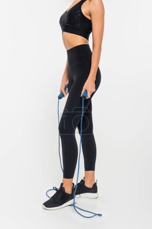 cropped view of fit sportswoman holding jump rope on white background, healthy and fit concept