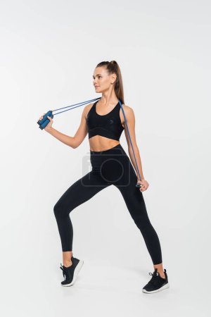 femme en vêtements de fitness tenant corde à sauter et posant sur fond blanc, endurance 