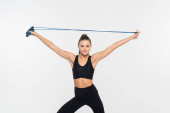 Fit sportswoman in fitness clothes holding skipping rope while looking at camera isolated on white Poster #664863080