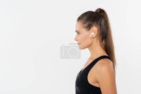 Foto de Vista lateral de la deportista en ropa deportiva negra usando auriculares inalámbricos aislados en blanco - Imagen libre de derechos