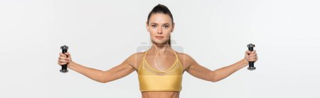 woman in sportwear looking at camera while training with dumbbells isolated on white, banner