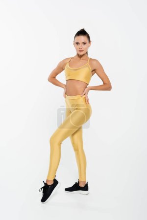 fit sportswoman in fitness clothes and sneakers, hands on hips, white background 