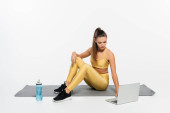 woman in active clothes using laptop while sitting near bottle and fitness mat on white background  t-shirt #664863680