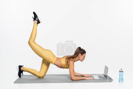 Photo for E-sports, sportswoman in active wear training near laptop on white background, physical activity - Royalty Free Image