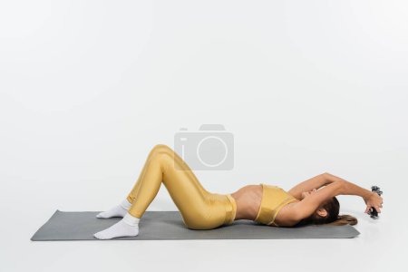 Foto de Mujer en calcetines y entrenamiento de ropa de fitness con mancuernas en la estera de fitness sobre fondo blanco - Imagen libre de derechos