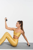sportswoman in yellow active wear working out, dumbbells, fitness mat, white background  Poster #664864148