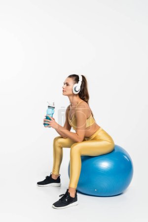 Téléchargez les photos : Mode de vie sain, aérobic, femme en tenue active et écouteurs sans fil assis sur la balle de fitness - en image libre de droit