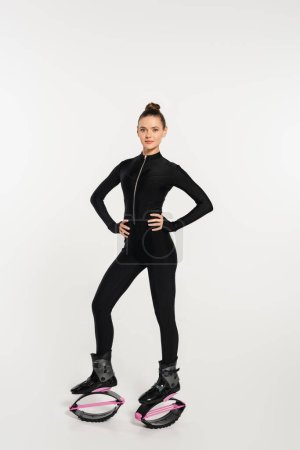 femme en bottes sautantes sur fond blanc, sportive avec corps tonique en combinaison noire