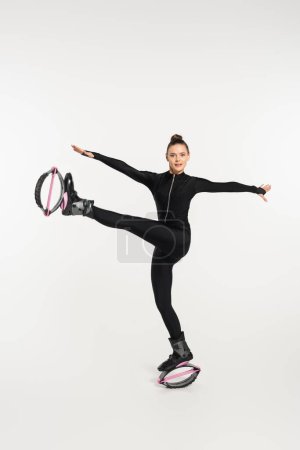 woman in jumping boots working out on white background, black jumpsuit and kangoo jumping shoes