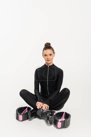 boots for jumping, sportswoman in black jumpsuit sitting with crossed legs, kangoo jumping, 
