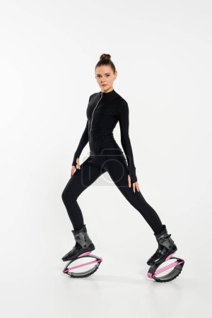 kangoo jumping concept, physical activity, woman in boots for jumping looking at camera on white 