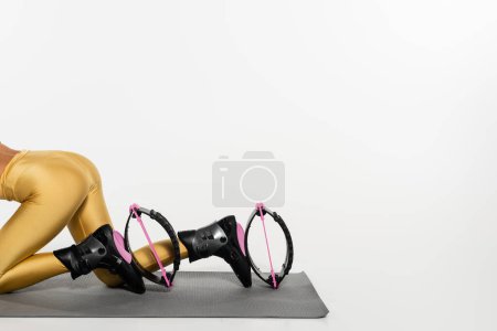 cropped view of woman in active wear exercising on fitness mat in kangoo jumping shoes, toned body 