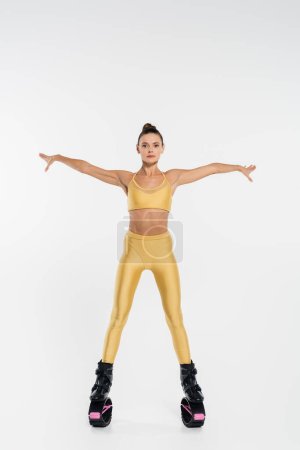 femme en vêtements de fitness portant des chaussures de saut kangoo, fond blanc, les mains tendues 