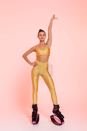 Frau in Sportbekleidung und Kangoo-Springschuhen, rosa Hintergrund, durchtrainierter Körper, Motivation und Energie 
