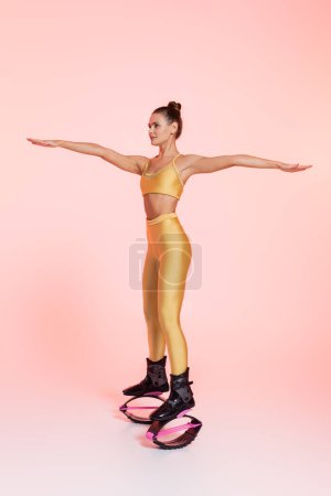 Foto de Entrenamiento divertido, mujer en botas de salto ejercicio sobre fondo rosa, tendencia, equilibrio y fuerza - Imagen libre de derechos