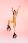 woman in kangoo jumping shoes exercising on pink background, raised hands, balance and strength  t-shirt #664866024
