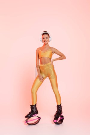 endurance, woman in kangoo jumping shoes and wireless headphones posing on pink background 