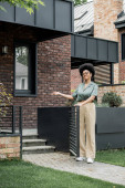 happy african american real estate broker pointing with hand and showing city cottage Poster #664923566