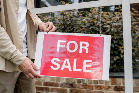 Téléchargez les photos : Vue partielle de l'agent immobilier suspendu enseigne avec à vendre lettrage à l'extérieur - en image libre de droit