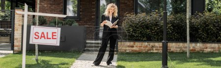 Téléchargez les photos : Pleine longueur de blonde agent immobilier avec dossier près de chalet et enseigne avec à vendre lettrage, bannière - en image libre de droit