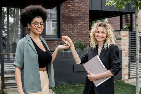 Blonde real estate agent giving key from new house to pleased african american buyer