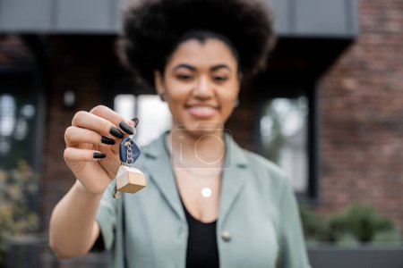 freudig afrikanisch-amerikanischer Immobilienmakler hält Schlüssel aus neuem Haus auf verschwommenem Hintergrund