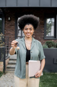 happy and successful african american real estate broker with folder holding key near new cottage Stickers #664924604