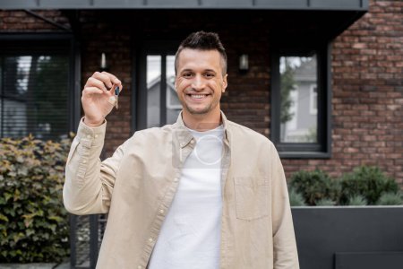 überglücklicher Immobilienmakler mit Schlüssel aus neuem Haus und lächelnd in die Kamera, Immobiliengeschäft