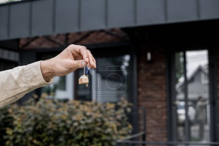 partial view of professional property agent holding key near modern cottage on blurred background Poster 664924642