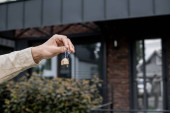 partial view of professional property agent holding key near modern cottage on blurred background hoodie #664924642
