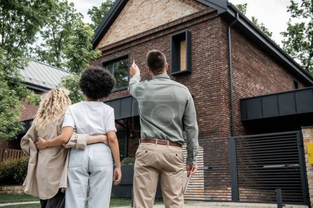 Blick zurück auf Immobilienmakler, der lesbischem Paar ein neues Haus im Freien zeigt