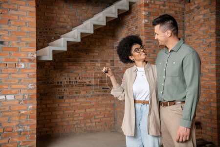 overjoyed african american woman holding keys and looking at man in new own house