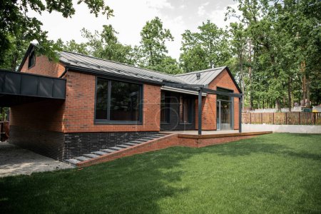 Téléchargez les photos : Maison en brique moderne avec de grandes fenêtres, pelouse verte, petite ville - en image libre de droit