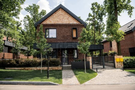 Téléchargez les photos : Maison spacieuse avec murs de briques et design moderne dans la ville de chalet, pelouse verte, arbres - en image libre de droit