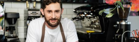 Téléchargez les photos : Portrait de barman barbu souriant en tablier regardant la caméra tout en travaillant dans un café, bannière - en image libre de droit