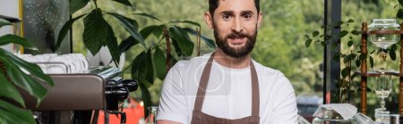 Photo for Cheerful bearded barista in apron looking at camera, standing and working in coffee shop, banner - Royalty Free Image