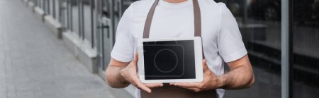 Photo for Cropped view of barista in apron holding digital tablet with blank screen on urban street, banner - Royalty Free Image