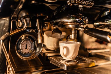 Foto de Vista de cerca del café que vierte de la máquina en taza blanca en la luz del sol en la cafetería - Imagen libre de derechos
