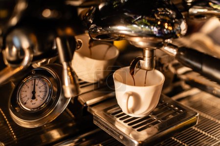 Téléchargez les photos : Vue rapprochée du café coulant de la machine dans une tasse blanche avec la lumière du soleil dans le café - en image libre de droit