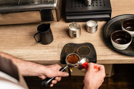 high angle view of barista holding press and holder with coffee in coffee shop