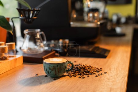 Tasse Cappuccino und Kaffeebohnen auf Arbeitsplatte in verschwommenem Café im Hintergrund