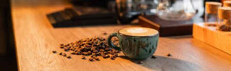 Tasse Cappuccino und Kaffeebohnen auf Arbeitsplatte in verschwommenem Café, Banner