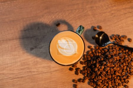 Draufsicht auf Tasse Cappuccino in der Nähe von Kaffeebohnen und Löffel auf Arbeitsplatte im Café