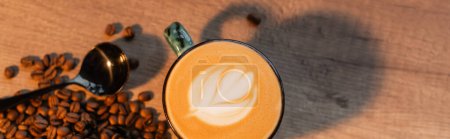 Photo for Top view of cup of cappuccino near coffee beans and spoon on table in cafe, banner - Royalty Free Image