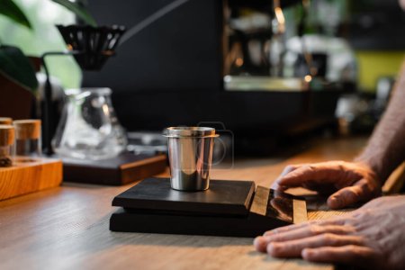 Foto de Vista recortada de barista de pie cerca de vaso de precipitados en balanzas electrónicas cerca de la máquina de café en la cafetería - Imagen libre de derechos